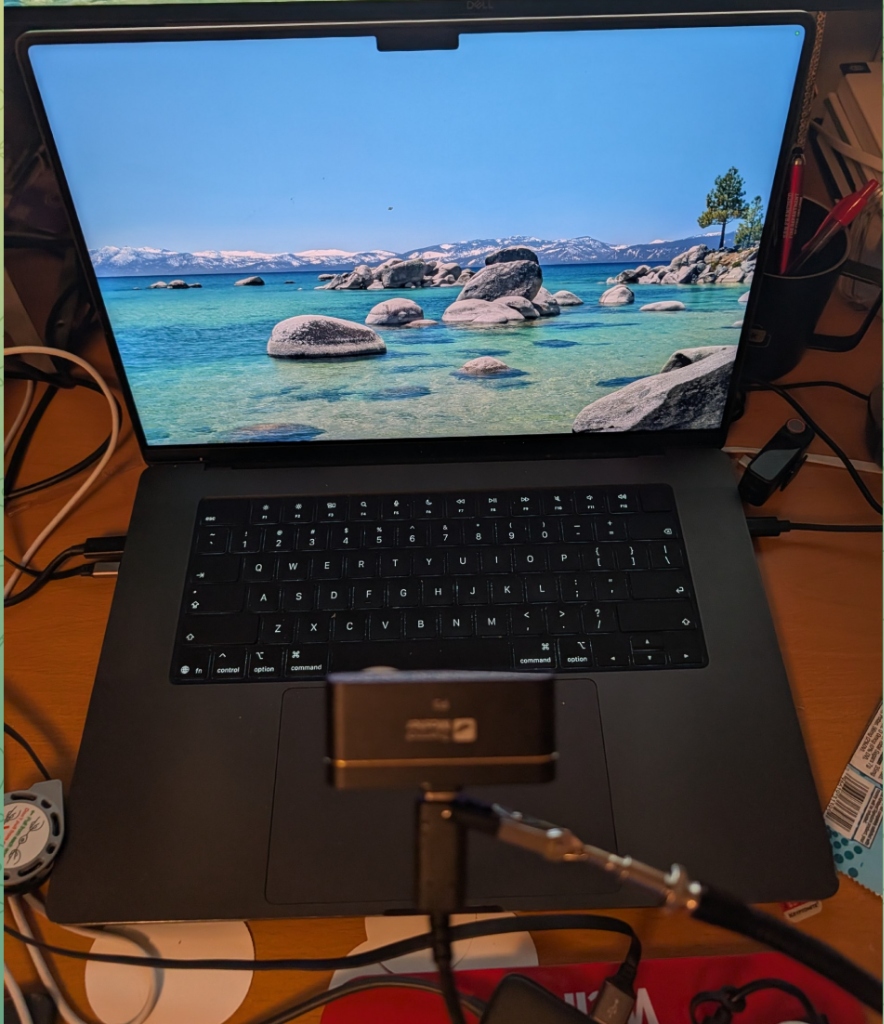 Photo of the Thermal Master P3 mounted on a rigid articulated arm looking down at the MacBook Pro M5 keyboard